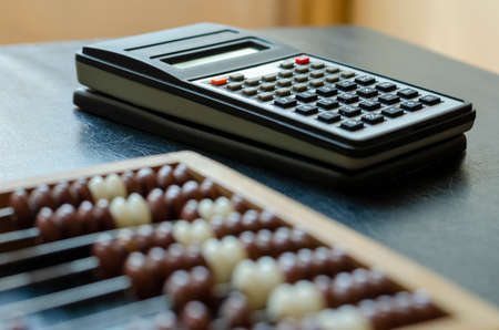 Close-up old wooden abacus and a calculator on a black table. An obsolete device for mathematical calculations and a modern device. Evolution Working tool of accountants, bookkeepers, mathematicians.の写真素材
