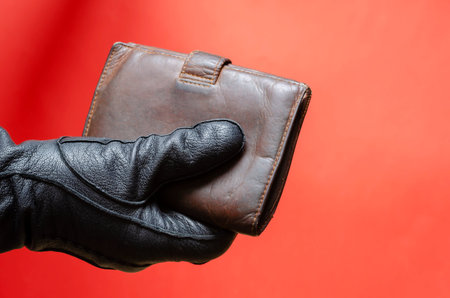 Hand in black leather glove holds out brown wallet. Male hand holds wallet to pay for purchase or...