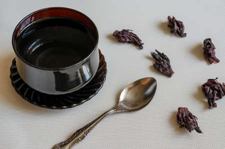 Black glass cup with boiling water, metal spoon and dry hibiscus petals. Dehydrated Sudanese rose for making hibiscus tea. Medicinal herbs. Selective focus.の写真素材