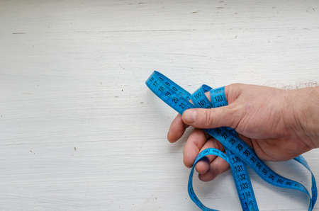 Male hand holds the blue measuring tape. Concept of life span, age. Middle-aged European man. Shooting from above over the shoulder. Selective focus.の写真素材