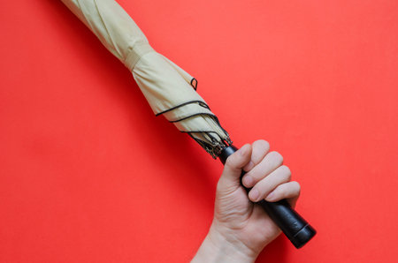 Male is holding an elegant light beige umbrella on coral background. Rain and wind protection...