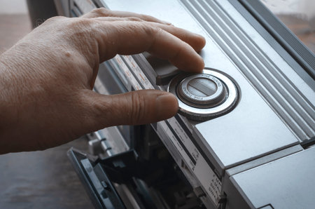 Adult Caucasian male hand tunes radio on retro stereo cassette recorder. Vintage audio equipment of...