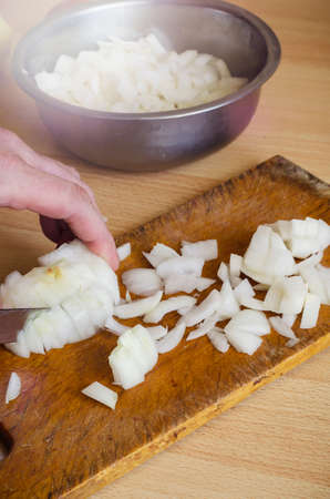 Male hand is cutting white onions on cutting board. Adult man of Caucasian ethnicity prepares food. Side view. Selective focus.の写真素材