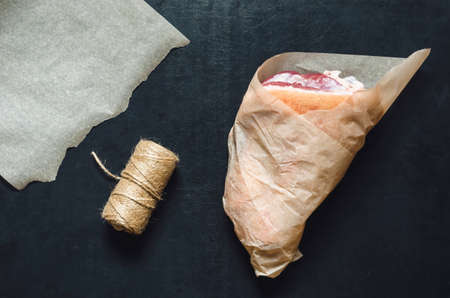 Raw pork knuckle wrapped in brown paper on black background. Eco-friendly packaging of products. Raw meat, butcher shop. View from above. Copy space. Selective focus.の写真素材