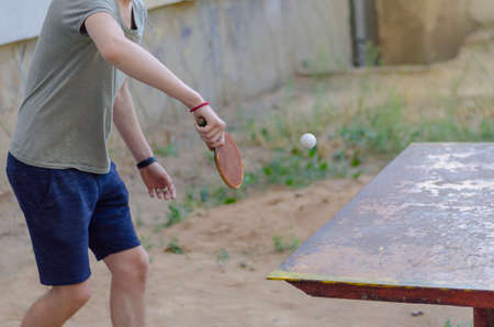Young Caucasian male playing table tennis outdoors. Metal tennis table for outdoor sports. Active lifestyle. Selective focus.の写真素材