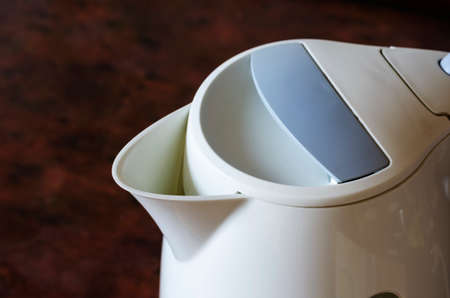 White electric kettle on the kitchen table. A plastic device for heating water on a maroon table. Top view at an angle. Selective focus.の写真素材