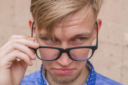 Blond man with small beard takes off his glasses in surprise.Young Man with funny Haircut in eye Glasses making grimace - funny face. Emotions, and signs concept.の写真素材