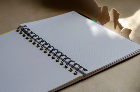 Open spring-bound notebook in sunlight. New diary with blank pages on torn wrapping paper. Side view...