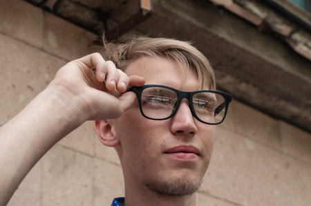 Portrait of a young man straightening his glasses. Handsome young man with fashionable hairstyle...
