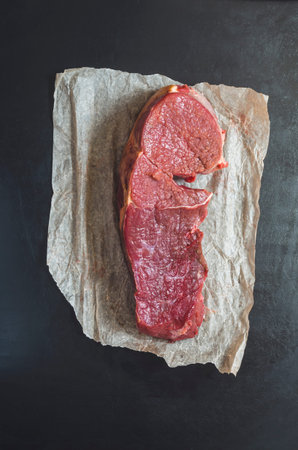 Raw beef tenderloin and wrapping paper on black background. Eco-friendly packaging of products. Raw...