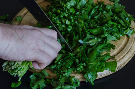 A male hand with a kitchen knife cuts the sorrel. Finely chopping green sorrel leaves on a wooden...