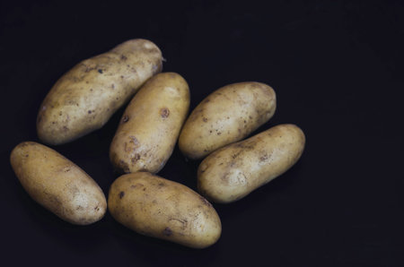 Raw potatoes in a peel on a black background. A portion of raw root vegetables. Cooking. Selective...