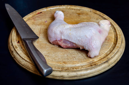 Raw chicken meat and kitchen knives on the chopping board. Chicken hip with hide. Cooking. Selective...