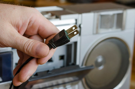 An adult caucasian male hand holds an electric plug of a retro stereo cassette recorder. Vintage...