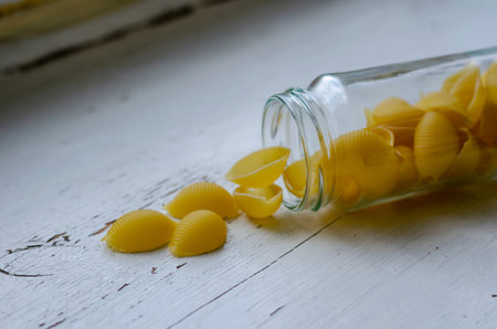 Raw Conchiglie Pasta in narrow glass jar on white wooden background. Close-up of serving of uncooked...