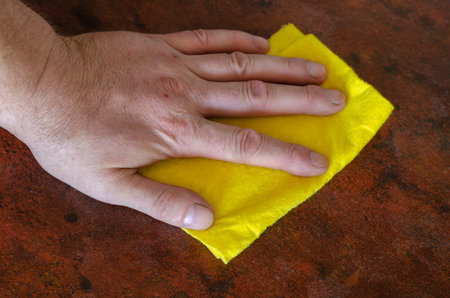 An adult male hand is wiping the kitchen table with a yellow rag. Home routine or commercial...
