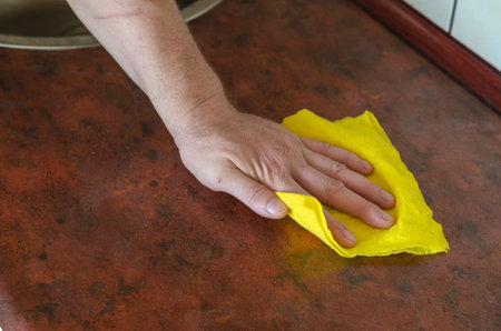 An adult male hand is wiping the kitchen table with a yellow rag. Home routine or commercial...