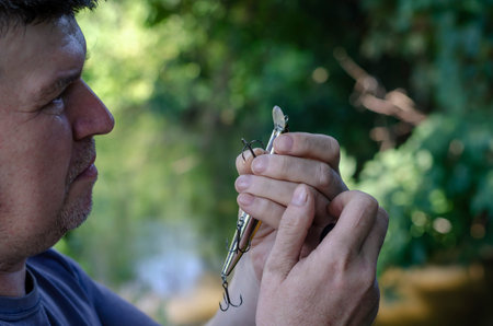 An adult man carefully examines a fishing hook on a wobbler. Artificial bait for catching predatory...