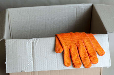 Protective gloves lie on an empty cardboard box. Open cardboard box for packaging. Services for the delivery and packaging of parcels. Selective focus.の写真素材