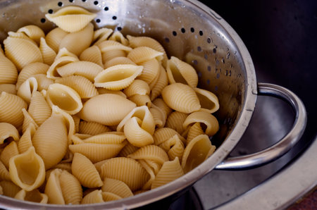Boiled Conchiglie in a metal colander. Close-up of a portion of ready-to-eat pasta. Traditional...