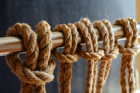 Metal pipe with repeating knots. Close-up of a railing with natural rope. Marine theme. Selective focus.の写真素材
