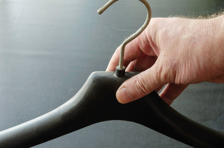 Male hand is holding a black plastic clothes hanger. Empty hanger for outerwear. Selective focus.