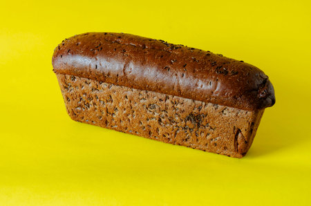 Loaf of rye bread with caraway seeds on a yellow background. Side view of freshly baked homemade...