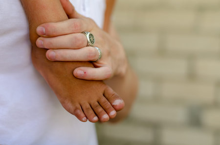 An adult young man's hand is holding the boy's leg. The bare foot of a mixed race preschooler and an...