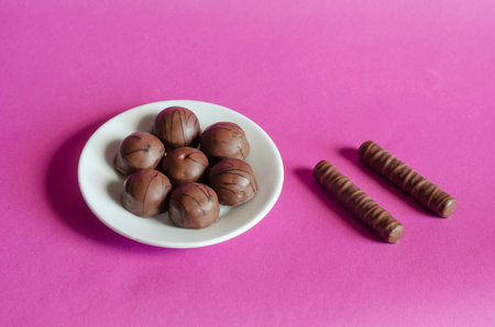 Random Chocolates in a white saucer on a pink background. Portion of assorted Confectionery. Sweet...