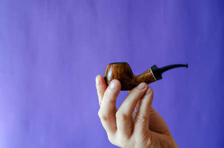 Briar root smoking pipe in hand. A man's hand holds a classic smoking pipe on a blue background. Selective focus.の写真素材