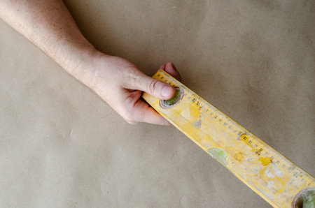 Hand of an adult Caucasian man holds a yellow construction level. A real hand tool with scratches...