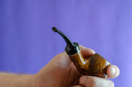 Briar root smoking pipe in hand. A man's hand holds a classic smoking pipe on a blue background....