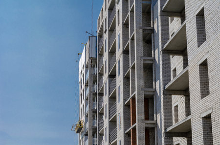 An unfinished skyscraper building against the blue sky. Facade works on heat and moisture insulation...