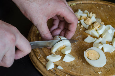 Male hands cut boiled chicken eggs on a wooden chopping board. Mature man cooks food. Selective...