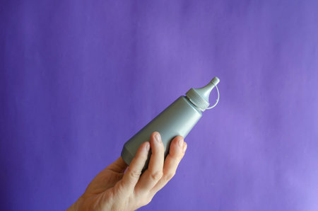 Male hand and gray plastic bottle of syrup. The man is holding a new bottle of sweet syrup for ice...