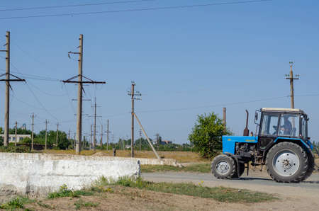 Nikolaev, Ukraine - September 15, 2020: A blue tractor drives along a rural road. The inscription in Russian means the name of the tractor. Agricultural engineering.の写真素材