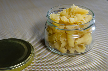 Glass jar with raw Gigli or campanelle pasta. Portion of uncooked pasta in a glass bowl on a beige...
