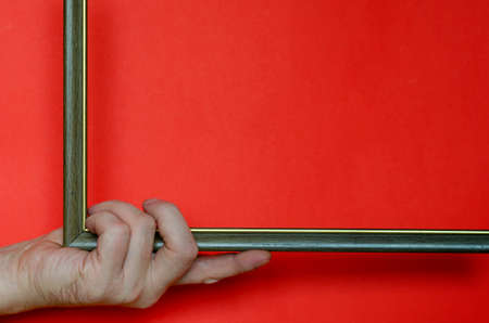 A male hand is holding an empty photo or picture frame on a red background. Bold multitasking background for various tasks with copy space. Minimalism.の写真素材