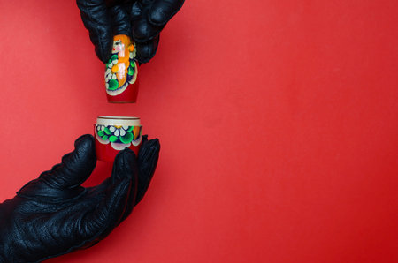 Hands of stranger in black leather gloves are taking apart wooden matryoshka doll. Russia symbol and...