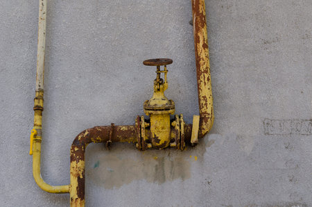 Old rusty yellow plumbing valve on a plastered wall. Gray wall with streaks. Outdated plumbing....