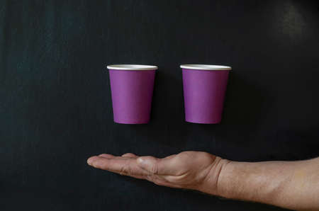 Creative background with paper cups for hot drinks and a man's hand. Hand and lilac glasses for coffee on a black background. Top view at an angle.の写真素材