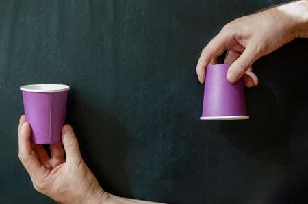 Creative background with paper cups for hot drinks and a man's hand. Hand and lilac glasses for coffee on a black background. Top view at an angle.の写真素材