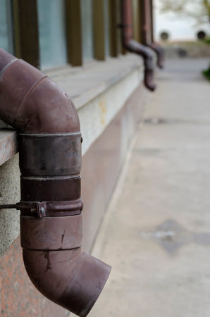 Facade of building with attached brown gutters. Row of plastic rain pipes in remote perspective....