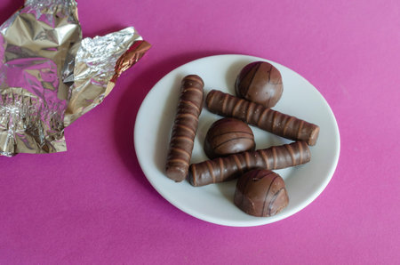 Chocolates, white saucer and candy wrapper on pink background. Portion of delicious ready-to-eat...