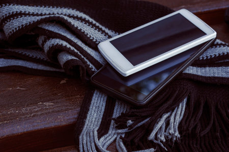 Concept of dating without phones and social networks. Two smartphones and striped scarf lie on park...