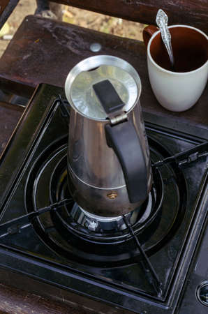Geyser metal coffee maker and portable gas stove on park bench. Process of making natural coffee during picnic or trip. Lifestyle.の写真素材