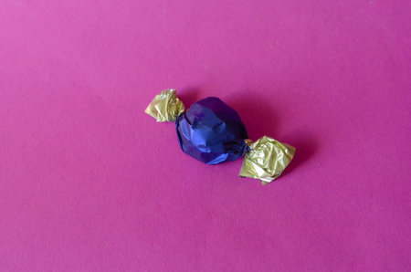 Single chocolate candy in two-color wrapper on pink. Sweet treat in foil wrapping close-up....