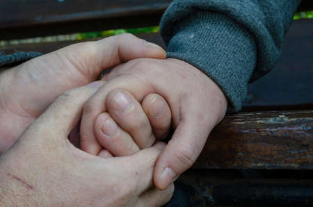Concept of love, loyalty, caring, tenderness, protection. Touching the male and female hands. Middle-aged man and woman touching each other sitting on park bench.の写真素材