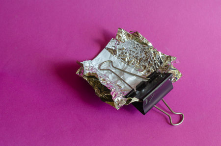 Smashed candy wrappers and Metal black Binder Clip on purple background. Binder Clip clamps random...