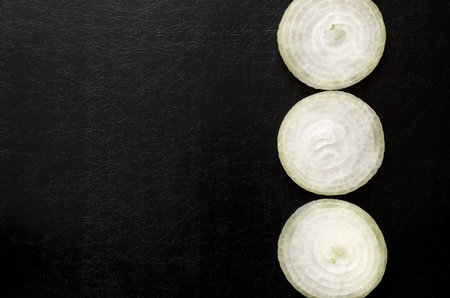 Raw bulb sliced with rings on black textured background. Three round pieces of white bulb. View from...